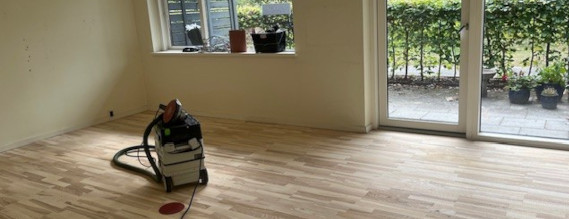 En tomt trægulv, hvor de står en masine til afslibning